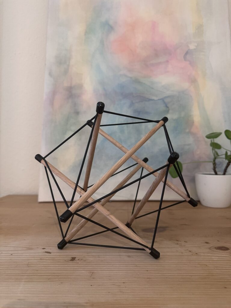 Tensegrity Modell vor einem Aquarell als Sinnbild für das Zusammenspiel von Zug- und Druckkräften